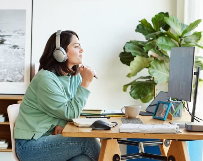 Vrouw met hoofdtelefoon en pen die op een pc-scherm kijkt