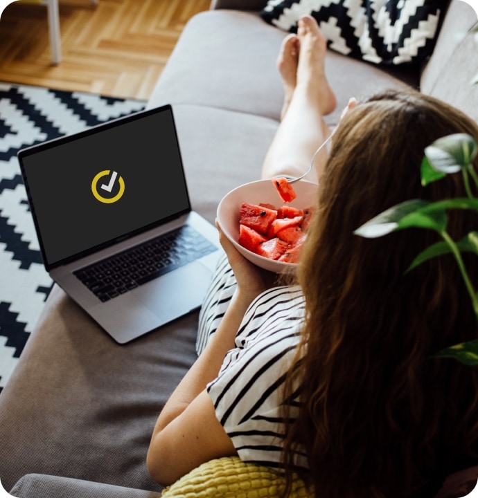 Vrouw die watermeloen eet op bank en met laptop waarop Norton 360 Antivirus Plus wordt gestart
